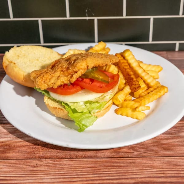 A fried chicken sandwich with lettuce, tomato, onion, and pickles, served with crinkle-cut fries.