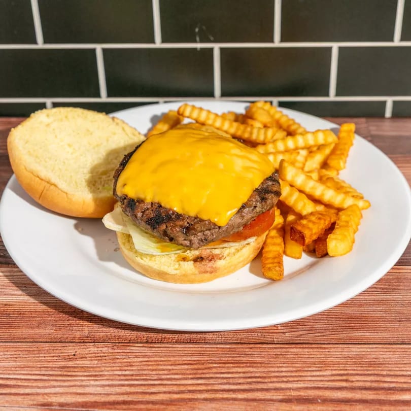 Cheeseburger with melted cheese, lettuce, tomato, and crinkle-cut fries on a white plate.