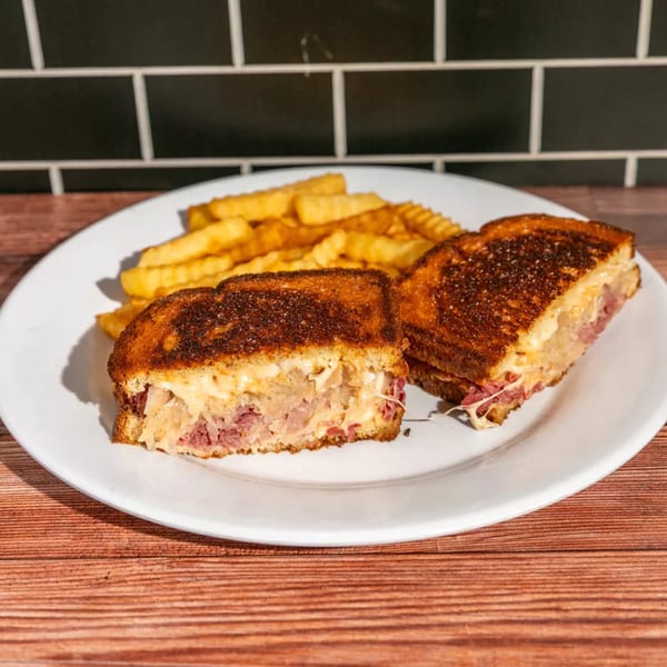 A grilled Reuben sandwich, cut in half, with fries on a white plate.