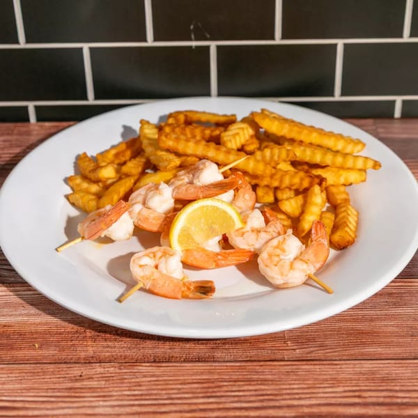 Shrimp skewers with crinkle-cut fries and a lemon wedge on a white plate.