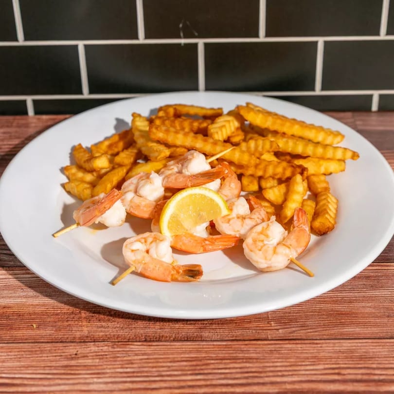 Shrimp skewers with crinkle-cut fries and a lemon wedge on a white plate.