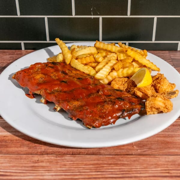 A plate of BBQ ribs with crinkle-cut fries and fried shrimp, garnished with a lemon wedge.