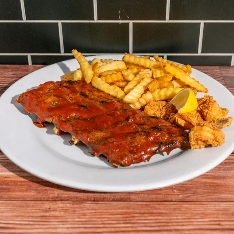 A plate of BBQ ribs with crinkle-cut fries and fried shrimp, garnished with a lemon wedge.